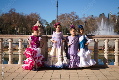 four pretty little girls dancing flamenco dressed in typical gypsy costume pose in a famous square in seville, spain. In the background a large fountain. Flamenco, cultural heritage of humanity.