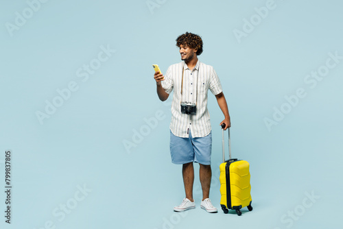 Full body traveler Indian man wear white casual clothes hold bag mobile cell phone isolated on plain blue background. Tourist travel abroad in free time rest getaway. Air flight trip journey concept. #799837805