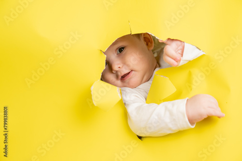 Cute Caucasian baby sticking out of a hole in a paper yellow background. 