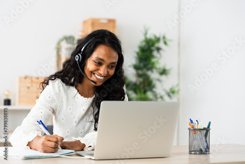 Positive telephone assistance worker talking on headset. Indian woman working from home.