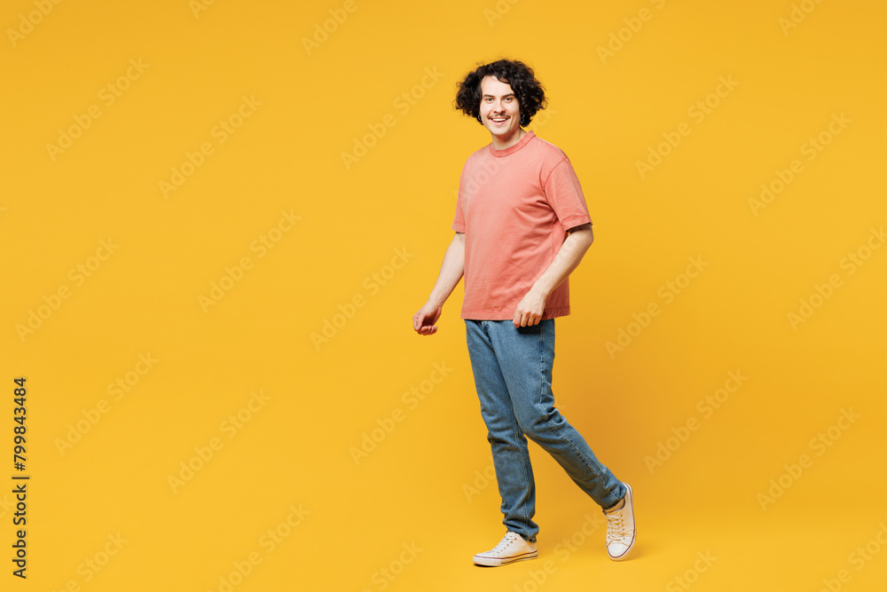 Full body side view young smiling cheerful fun happy man he wears pink t-shirt casual clothes walking going look camera isolated on plain yellow orange background studio portrait. Lifestyle concept. Full body side view young smiling cheerful fun happy man he wears pink t-shirt casual clothes walking going look camera isolated on plain yellow orange background studio portrait. Lifestyle concept.