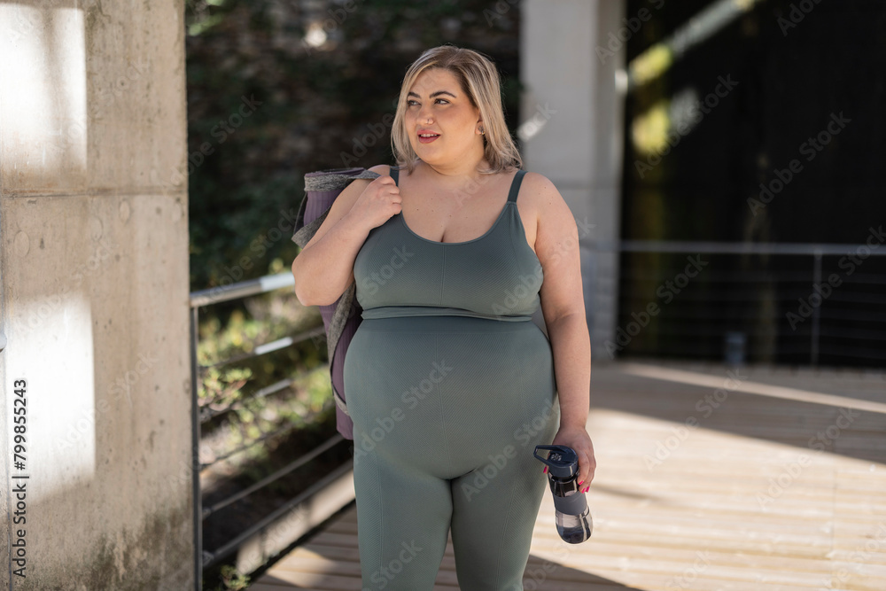 Curvy young woman with water bottle standing on footbridge Curvy young woman with water bottle standing on footbridge