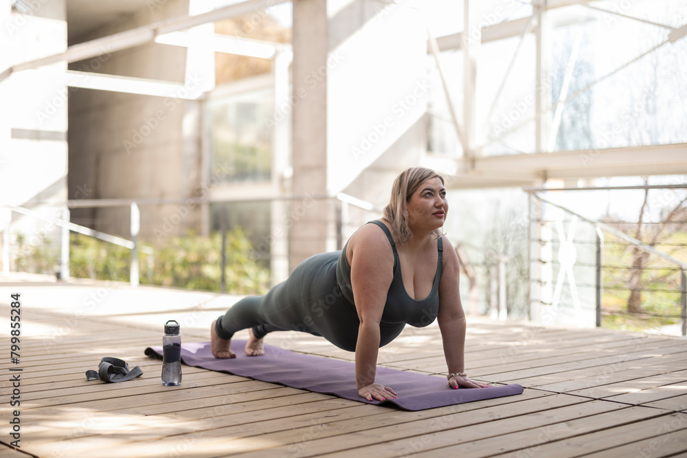 Young curvy woman practicing plank pose on mat in park Young curvy woman practicing plank pose on mat in park