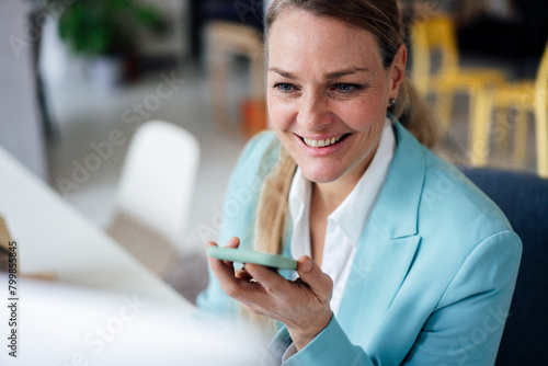 Wallpaper Mural Smiling mature businesswoman talking through smart phone speaker at office Torontodigital.ca