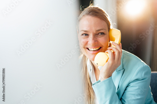 Happy businesswoman talking through telephone receiver in office photo