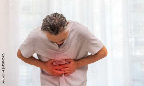 Senior asian elderly man sick unhappy touching belly stomach with suffering from stomach ache pain, gastritis, gastroenteritis, food poisoning, diarrhea, intestinal inflammation at home photo