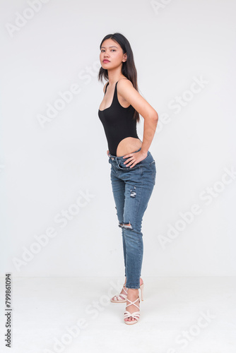 A tall sexy young asian woman in a black bodysuit and ripped jeans Isolated on a white background. Hands on hips, slightly leaning forward. Whole body photo. © Mdv Edwards