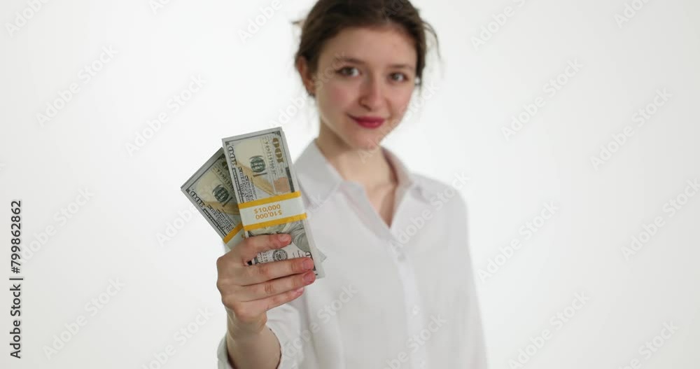Satisfied woman holds stacks of dollar banknotes in hand looking in camera and smiling. Young manager shows profit from startup successful deal slow motion Satisfied woman holds stacks of dollar banknotes in hand looking in camera and smiling. Young manager shows profit from startup successful deal slow motion