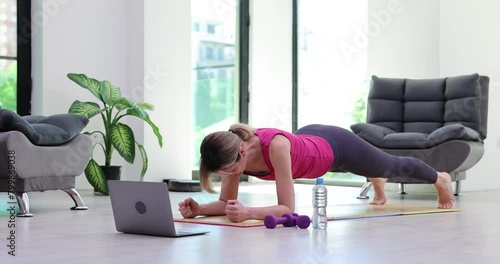 Fit woman does yoga plank pose following online lesson on mat maintaining body in light premise. Exercise to improve core of back and straight posture concept photo