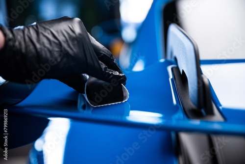 Car cash or car detailing studio worker applying graphene or ceramic coating on blue sport car.