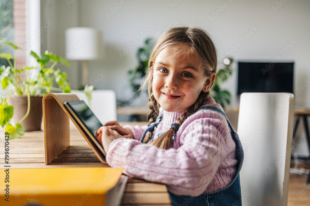 Smiling girl sitting with tablet PC at table at home Smiling girl sitting with tablet PC at table at home