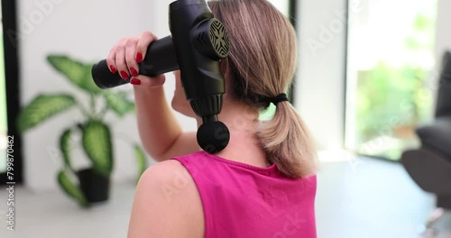 Woman massages neck and shoulders with modern massager. Device for relaxing body after monotonous work. Office worker relaxes back after long work in sitting position