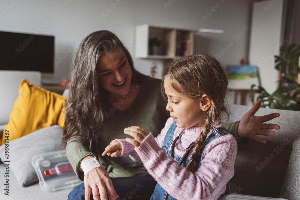 Granddaughter wrapping bandage on happy grandmother's wrist sitting on sofa at home Granddaughter wrapping bandage on happy grandmother's wrist sitting on sofa at home