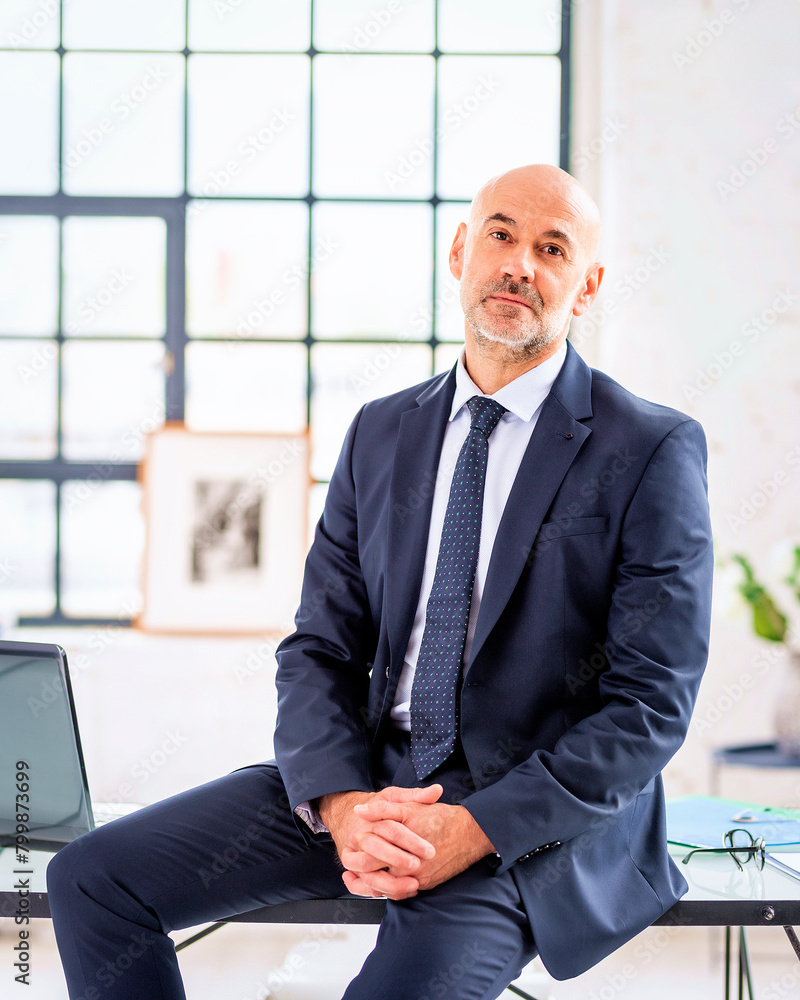 Mid aged businessman wearing suit and sitting at office desk Mid aged businessman wearing suit and sitting at office desk