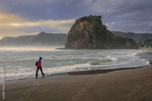 Person walking on a sandy beach at the shoreline at sunset, Piha, Auckland, New Zealand.