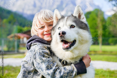 Smiling blond boy hugging Husky dog photo