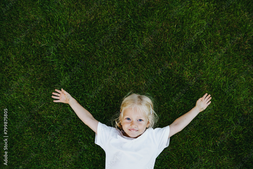 Smiling blond girl with arms outstretched lying down on grass Smiling blond girl with arms outstretched lying down on grass