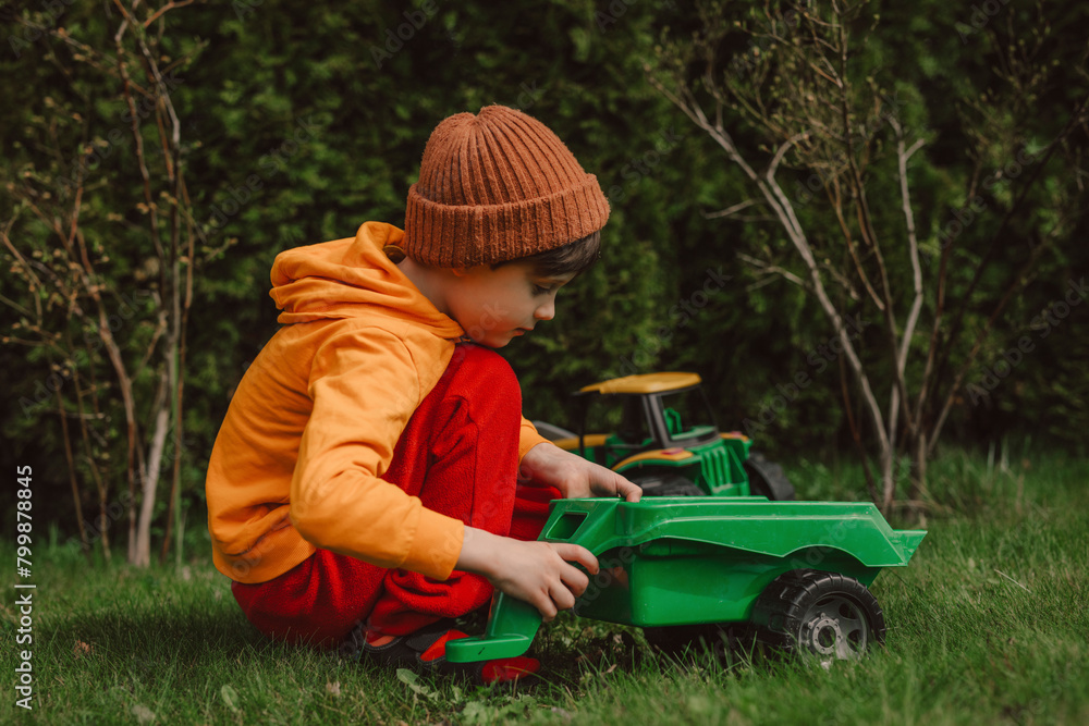 Boy crouching and playing with green toy tractor on grass in back yard