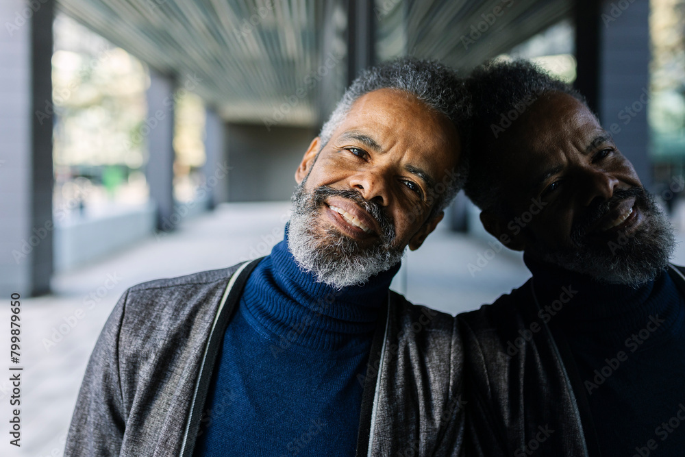 Smiling mature businessman leaning on glass wall