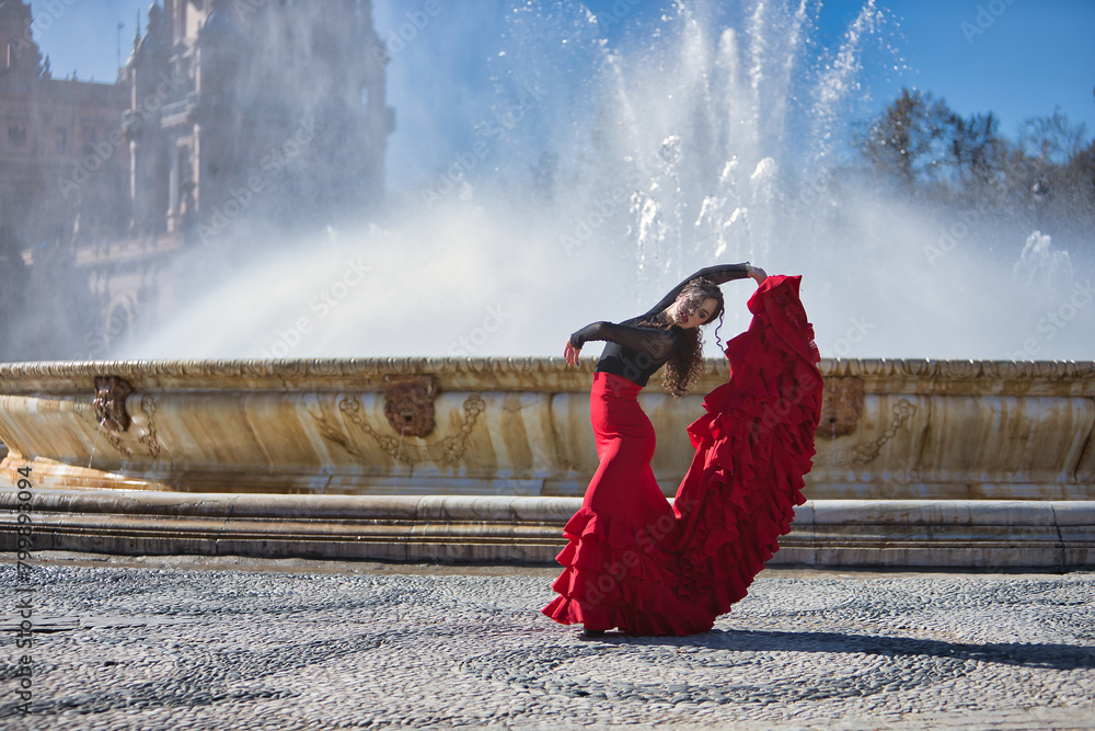 Fototapeta premium Young, beautiful, brunette woman in black shirt and red skirt, dancing flamenco in front of a beautiful fountain in Spain square in Seville. Flamenco concept, dance, art, typical Spanish.