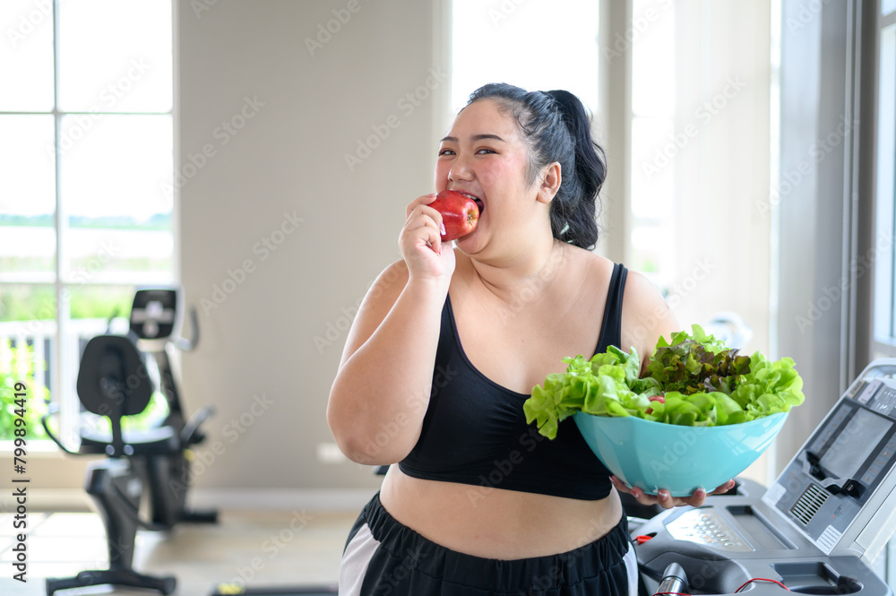 Overweight Asian female happy to eat organic apple for healthy in gym. Weight loss workout, healthy lifestyle concept. Overweight Asian female happy to eat organic apple for healthy in gym. Weight loss workout, healthy lifestyle concept.