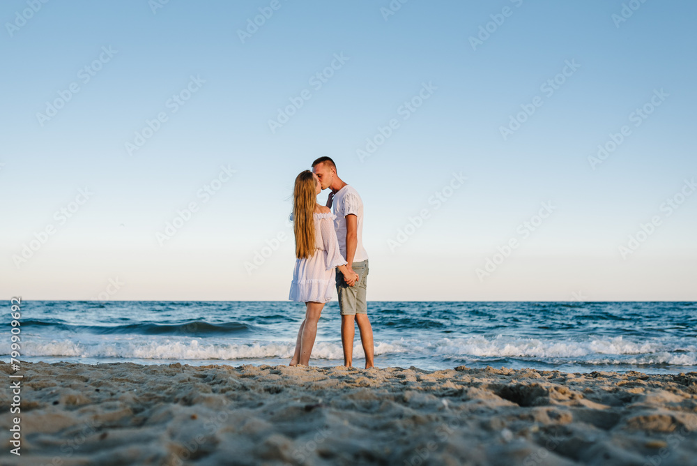 Female kiss and hugs male stand barefoot on beach ocean and enjoy sunny summer day on vacation. Couple in love hugging and kissing on seashore. Man embraces woman walk on sand sea. Spend time together