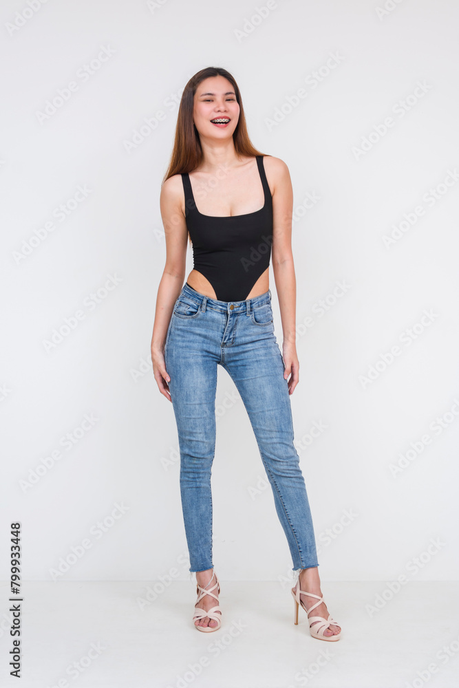 Young Asian woman in black bodysuit and jeans smiling against white background Young Asian woman in black bodysuit and jeans smiling against white background