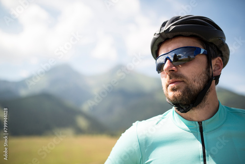 Portrait of attractive male cyclist, riding bike across beautiful nature, wearing helmet, sunglasses. Concept of healthy lifestyle. © Halfpoint