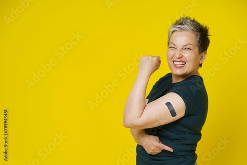 Senior grey haired woman rebelling showing nude shoulder with dark band aid plaster it isolated yellow background amazing mature woman 50s vaccination healthcare concept