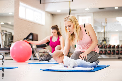 Baby movement class. Parents helping babies to improve motor skills, proper movement on fitball. Pediatric physical therapist leading class. Mothers exercising with babies.