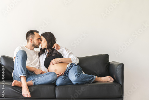 Pregnant couple embracing on a black sofa in a modern living room