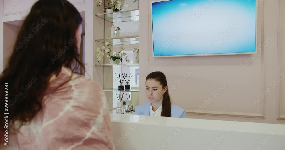 A young woman interacts with a receptionist at a chic beauty clinic, highlighting customer service and modern interior. Young Woman Talking to Receptionist at Modern Beauty Clinic A young woman interacts with a receptionist at a chic beauty clinic, highlighting customer service and modern interior. Young Woman Talking to Receptionist at Modern Beauty Clinic