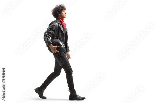Full length profile shot of a of a young man in leather jacket walking and holding a motorbike helmet