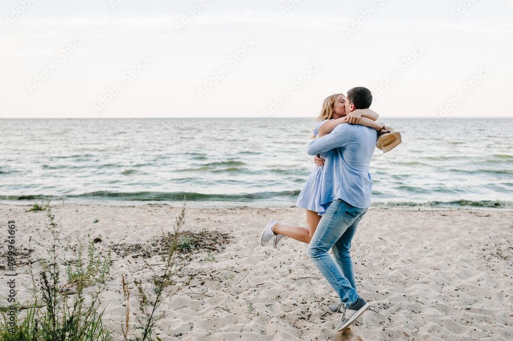 Female kisses male on beach ocean and enjoys sunny summer day. Man embraces woman stands on sand sea. Couple in love hugging and kissing each other on seashore. Spending time together. Female kisses male on beach ocean and enjoys sunny summer day. Man embraces woman stands on sand sea. Couple in love hugging and kissing each other on seashore. Spending time together.