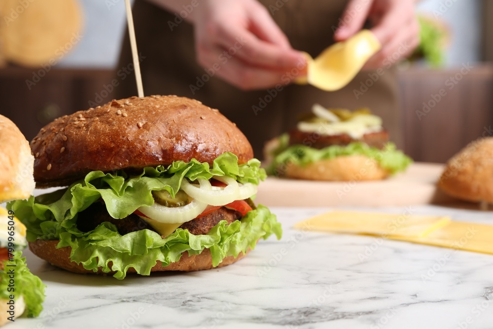 Woman making delicious vegetarian burger at white marble table, selective focus