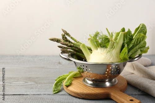 Metal colander with fennel, lettuce and asparagus on gray wooden table, space for text
