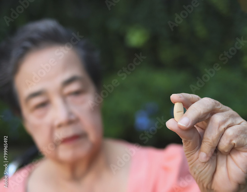  senior woman holding medical pill r in the garden, showing medicine to camera, selective focus on the pill.