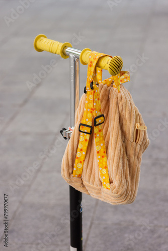 A child's backpack hangs on the handlebars of a scooter