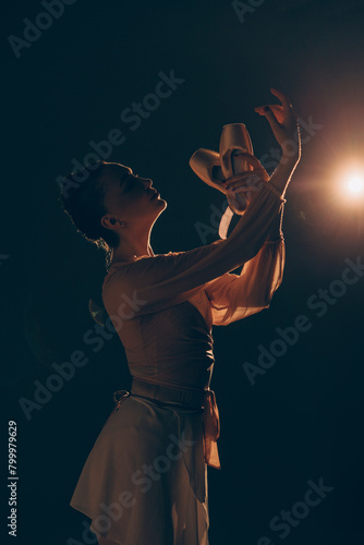 Closeup view to young ballerina holding pointe shoes in her hands on dark background against light.