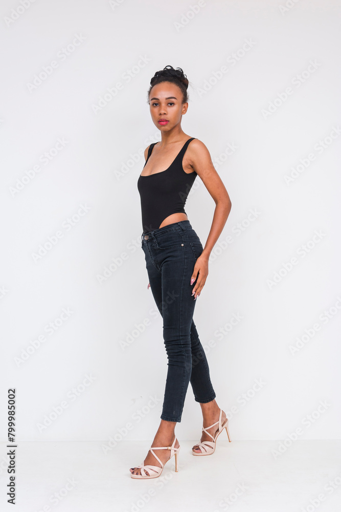 Confident mixed-ancestry woman in black bodysuit poses stylishly against a white backdrop Confident mixed-ancestry woman in black bodysuit poses stylishly against a white backdrop