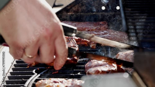 Watch the video of grilling steaks on a gas grill for a delicious cooking experience. Ribeye or pork steaks are prepared with tongs, showcasing the art of grilling cuisine photo