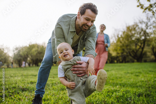 First steps for little toddler. Father supporting baby while walking in soft spring grass on meadow. Father's day concept. © Halfpoint
