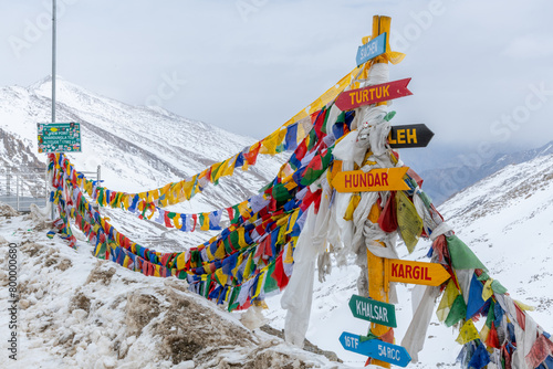 Prayer flags and signpost at the summit of Khardung La pass, at 17,582 feet one of the world's highest motorable roads in India