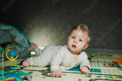 Photo of a 7-9 month old baby at home. A smiling child lies on the floor and plays with toys. Cute boy sitting on the floor.