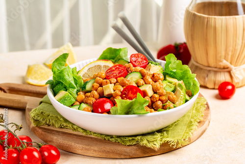 Kitchen table with mediterranean chickpea salad. Chickpea and paprika baked beans, lettuce, tomatoes, avocado, cucumber, lemon and olive oil dressing. Healthy high protein vegan meal.