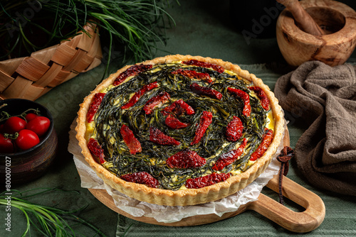 Italian rustic savory pie made with pie crust, salsola soda or agretti, ricotta cheese, eggs and dried tomatoes on a green wooden table. Homemade baked food.