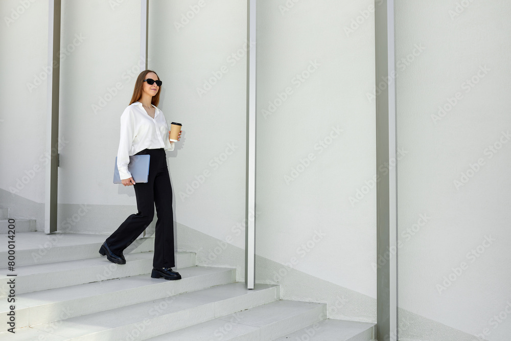 A stylish business lady walks up the stairs to her office and drinks coffee. Laptop in hand. A successful person A stylish business lady walks up the stairs to her office and drinks coffee. Laptop in hand. A successful person