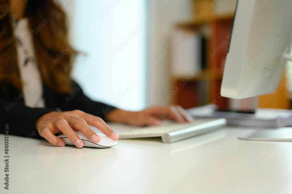 Fototapeta premium Cropped shot of female manager clicking wireless computer mouse and typing on keyboard