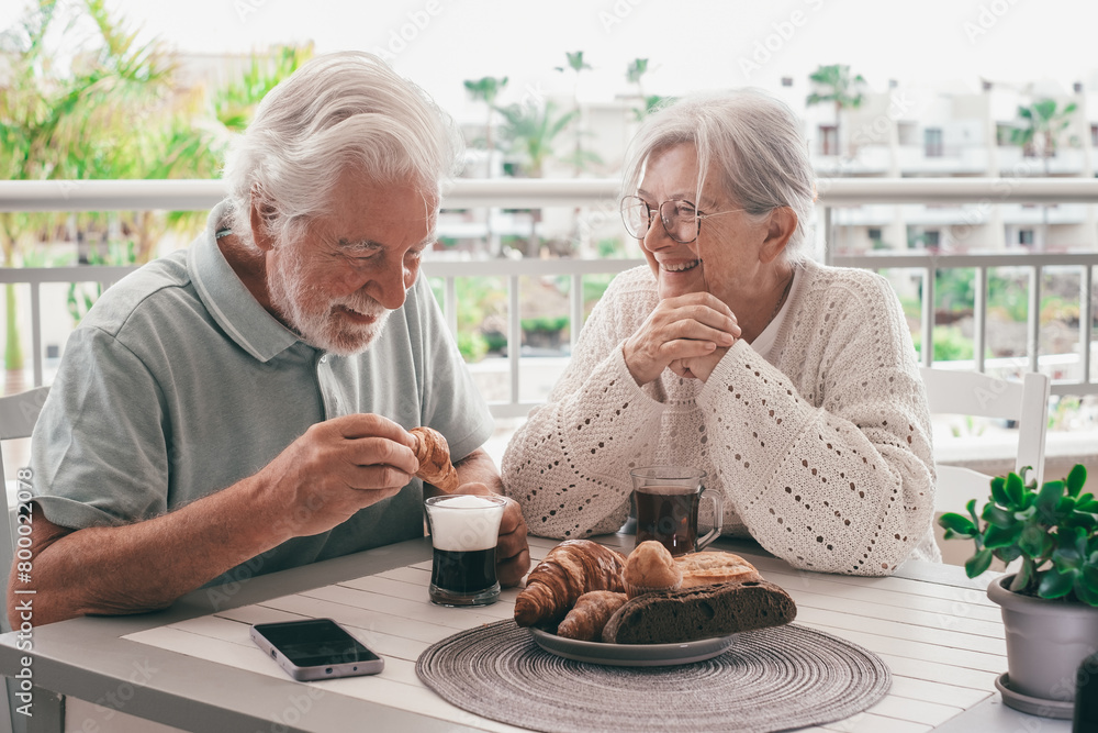 Cheerful bonding senior retired couple enjoy breakfast together sitting outdoors on home terrace. Serene retirement lifestyle concept Cheerful bonding senior retired couple enjoy breakfast together sitting outdoors on home terrace. Serene retirement lifestyle concept