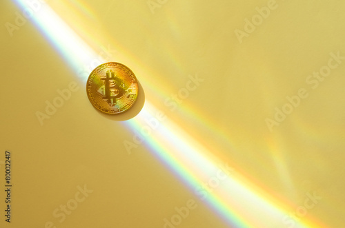 Gold bitcoin on a yellow background with a rainbow, copy space.
